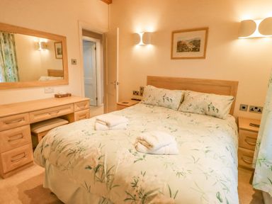 A bedroom with a double bed and floral bedding a wooden dresser with a mirror and bedside tables at Tanglewood Lodge Thirlmere 15 White Cross Bay near Windermere