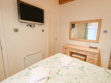 A bedroom with a wall-mounted TV a dresser with a mirror and a bed with folded towels at Tanglewood Lodge Thirlmere 15 White Cross Bay near Windermere