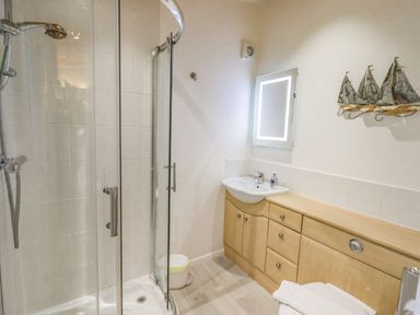 A bathroom with a shower enclosure sink with cabinet and illuminated mirror at Tanglewood Lodge Thirlmere 15 White Cross Bay near Windermere