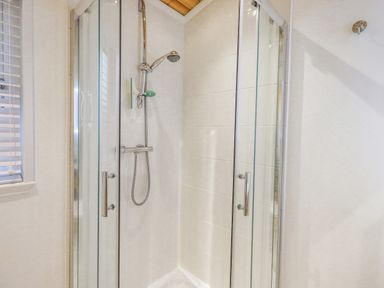 A shower enclosure with glass doors and a wall-mounted showerhead at Tanglewood Lodge in Thirlmere 15 White Cross Bay near Windermere