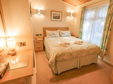 A bedroom with a double bed two bedside tables lamps curtains and a window at Tanglewood Lodge Thirlmere 15 White Cross Bay near Windermere