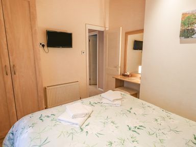 A bedroom with a bed covered with floral bedding two sets of folded towels on the bed a wall-mounted tv a wooden wardrobe and a dressing table with a mirror at Tanglewood Lodge Thirlmere 15 White Cross Bay near Windermere