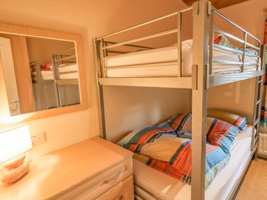 A bedroom with a metal bunk bed and a wooden dresser with a lamp and a mirror at Tanglewood Lodge Thirlmere 15 White Cross Bay near Windermere