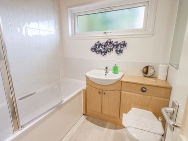 A bathroom with a bathtub and shower screen a sink with green soap on a wooden cabinet and a toilet with a towel on the seat at Tanglewood Lodge Thirlmere 15 White Cross Bay near Windermere