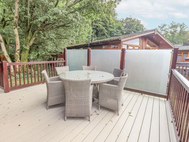 An outdoor deck with a round table and six wicker chairs surrounded by wooden railings at Tanglewood Lodge Thirlmere 15 White Cross Bay near Windermere