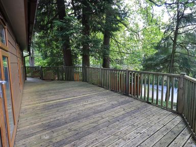 A wooden deck with railing outside a house surrounded by trees at Forest Pines Lodge Beech Hill 10 Fallbarrow Park near Bowness on Windermere