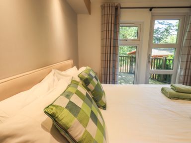A bedroom with a bed with green checkered pillows and folded towels by a window at Forest Pines Lodge Beech Hill 10 Fallbarrow Park near Bowness on Windermere