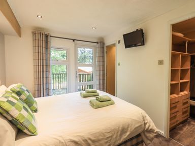 A bedroom with a bed with green plaid pillows towels on the bed a wall-mounted tv and an open closet with shelves and drawers at Forest Pines Lodge Beech Hill 10 Fallbarrow Park near Bowness on Windermere