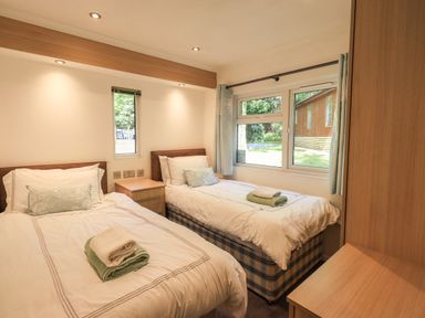 A bedroom with two single beds and a window showing a garden at Forest Pines Lodge in Beech Hill 10 Fallbarrow Park near Bowness on Windermere