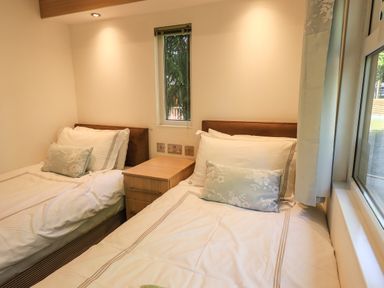 A bedroom with two single beds separated by a wooden nightstand with three drawers at Forest Pines Lodge Beech Hill 10 Fallbarrow Park near Bowness on Windermere