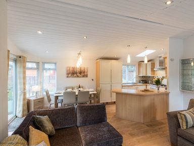An open plan living area with a kitchen island dining table set and sofas at Broad Larch Lodge in Glade 16 Fallbarrow Park near Bowness on Windermere