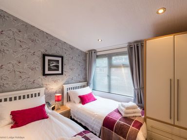 A bedroom with two single beds bedside table with lamp and wardrobe at Broad Larch Lodge in Glade 16 Fallbarrow Park near Bowness on Windermere