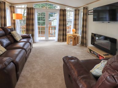 A living room with leather sofas a fireplace a wall-mounted tv and large windows at Squirrels Snug in Pony Meadow 1 White Cross Bay near Windermere