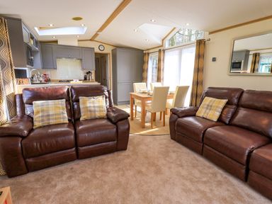A living room with two brown leather sofas and a dining table with four chairs near grey kitchen cabinets at Squirrels Snug in Pony Meadow 1 White Cross Bay near Windermere