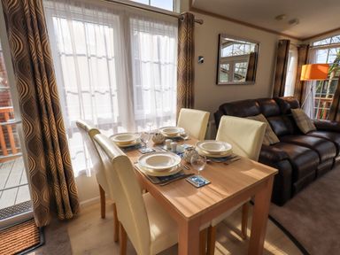 A dining table set for four with white chairs next to a brown leather sofa in a living room at Squirrels Snug in Pony Meadow 1 White Cross Bay near Windermere