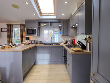 A kitchen with grey cabinets wooden countertops a microwave sink window and kitchen appliances at Squirrels Snug in Pony Meadow 1 White Cross Bay near Windermere