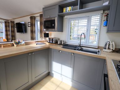 A kitchen with grey cabinets a wooden countertop a microwave toaster kettle and a sink with a window at Squirrels Snug in Pony Meadow 1 White Cross Bay near Windermere