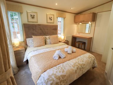 A bedroom with a double bed bedside tables lamps and a dressing table at Squirrels Snug in Pony Meadow 1 White Cross Bay near Windermere