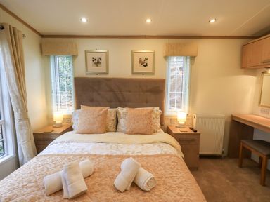 A bedroom with a bed pillows and rolled towels two bedside tables with lamps and a dressing table with a stool at Squirrels Snug in Pony Meadow 1 White Cross Bay near Windermere