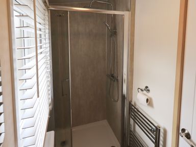 A bathroom with a glass shower enclosure a showerhead a wall-mounted toilet paper holder and a towel radiator at Squirrels Snug in Pony Meadow 1 White Cross Bay near Windermere