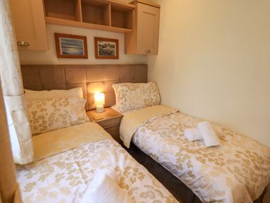 A bedroom with two single beds with floral bedding a nightstand and lamp between the beds and two framed pictures on the wall at Squirrels Snug Pony Meadow 1 White Cross Bay near Windermere