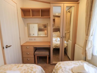 A bedroom with two single beds a desk with three drawers a stool a wall-mounted shelf and a double-door wardrobe with mirrors at Squirrels Snug in Pony Meadow 1 White Cross Bay near Windermere