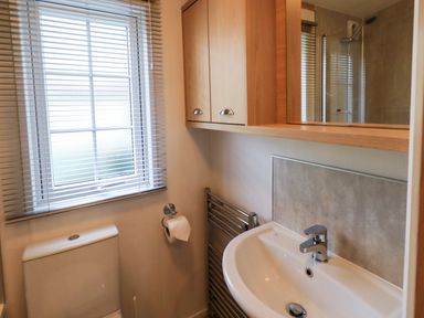 A bathroom with a window with blinds a toilet a sink a towel rail and a cabinet above the sink at Squirrels Snug in Pony Meadow 1 White Cross Bay near Windermere