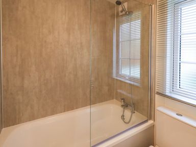 A bathroom with a bathtub shower and a window with blinds at Squirrels Snug in Pony Meadow 1 White Cross Bay near Windermere