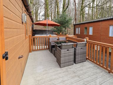 An outdoor wooden deck with a table and chairs and an umbrella at Squirrels Snug in Pony Meadow 1 White Cross Bay near Windermere