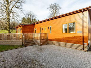 A wooden cabin with a porch and steps surrounded by gravel and trees at Comraich Beckside 40 Limefitt Park near Windermere