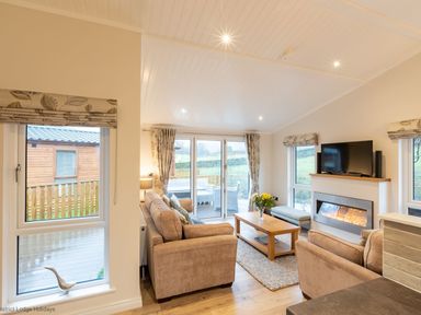 A living room with beige sofas a wooden coffee table a fireplace and a TV at Comraich Beckside 40 Limefitt Park near Windermere