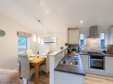 A kitchen and dining area with a wooden dining table set for four and kitchen appliances at Comraich Beckside 40 Limefitt Park near Windermere