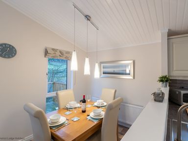 A dining area with a wooden table set for four with cream chairs and pendant lights at Comraich Beckside 40 Limefitt Park near Windermere