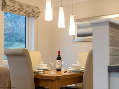 A dining table set with glasses bowls and a bottle of wine in a room at Comraich Beckside 40 Limefitt Park near Windermere