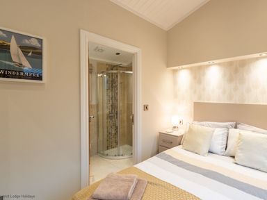 A bedroom with a bed pillows side table with lamp and an open door showing a bathroom with a shower at Comraich Beckside 40 Limefitt Park near Windermere