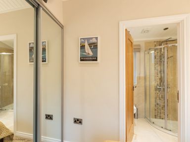 A bathroom with a glass shower enclosure seen through an open wooden door and a mirrored wardrobe door on the left wall at Comraich Beckside 40 Limefitt Park near Windermere