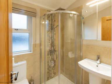 A bathroom with a glass shower enclosure a toilet a sink and a window at Comraich Beckside 40 Limefitt Park near Windermere
