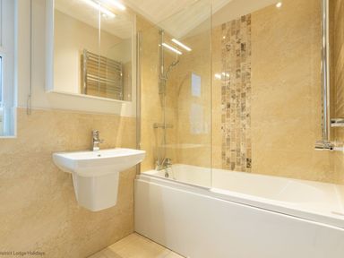 A bathroom with a sink a bathtub a showerhead and tiled walls at Comraich Beckside 40 Limefitt Park near Windermere