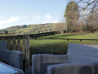 An outdoor seating area with wicker chairs overlooking a green field and hills at Comraich in Beckside 40 Limefitt Park near Windermere