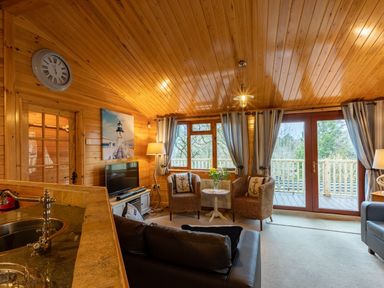 A living room with wicker chairs and a small table near windows and glass doors at Lakeshaven Skiptory Howe 16 White Cross Bay near Windermere
