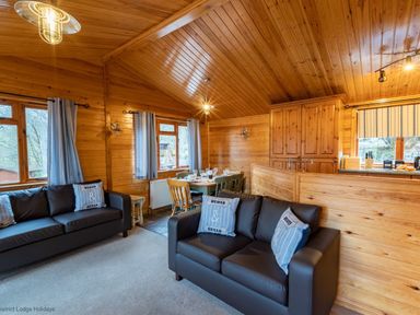 A living room with two black sofas and pillows next to a dining table and wooden kitchen cabinets at Lakeshaven Skiptory Howe 16 White Cross Bay near Windermere
