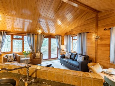 A wooden living room with a black sofa, two wicker chairs, a lamp, and a kitchen sink at Lakeshaven Skiptory Howe 16 White Cross Bay near Windermere