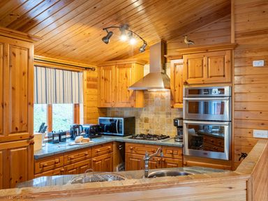 A kitchen with wooden cabinets a stove microwave coffee maker and toaster at Lakeshaven Skiptory Howe 16 White Cross Bay near Windermere