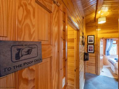 A wooden hallway with a sign pointing to the poop deck and a bedroom with blue curtains at Lakeshaven Skiptory Howe 16 White Cross Bay near Windermere