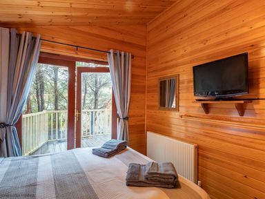 A bedroom with a bed and folded towels near glass doors opening to a balcony with trees outside at Lakeshaven Skiptory Howe 16 White Cross Bay near Windermere