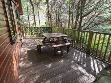 A wooden deck with a picnic table and benches surrounded by trees at Lakeshaven Skiptory Howe 16 White Cross Bay near Windermere