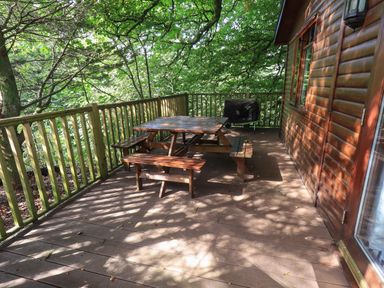 A wooden deck with a picnic table and benches beside a wooden cabin surrounded by trees at Lakeshaven Skiptory Howe 16 White Cross Bay near Windermere