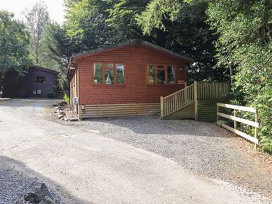 A wooden cabin with a gravel driveway surrounded by trees at Lakeshaven Skiptory Howe 16 White Cross Bay near Windermere