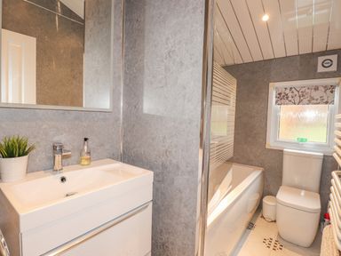 A bathroom with a sink and mirror on the left and a bathtub, toilet, and window on the right at Limefitt Lodge Fellside 8 Limefitt Park near Windermere