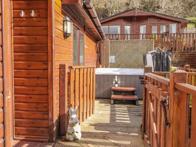 A wooden deck with a hot tub steps and a welcoming rabbit statue at Limefitt Lodge Fellside 8 Limefitt Park near Windermere